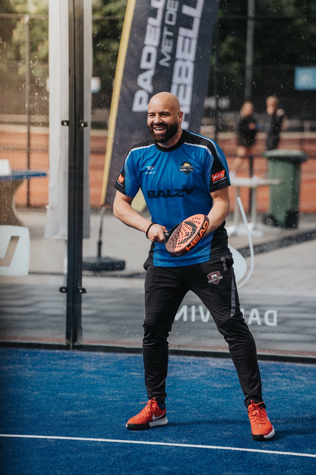 Rebel in blauw wedstrijdshirt lacht midden op de blauwe padelbaan