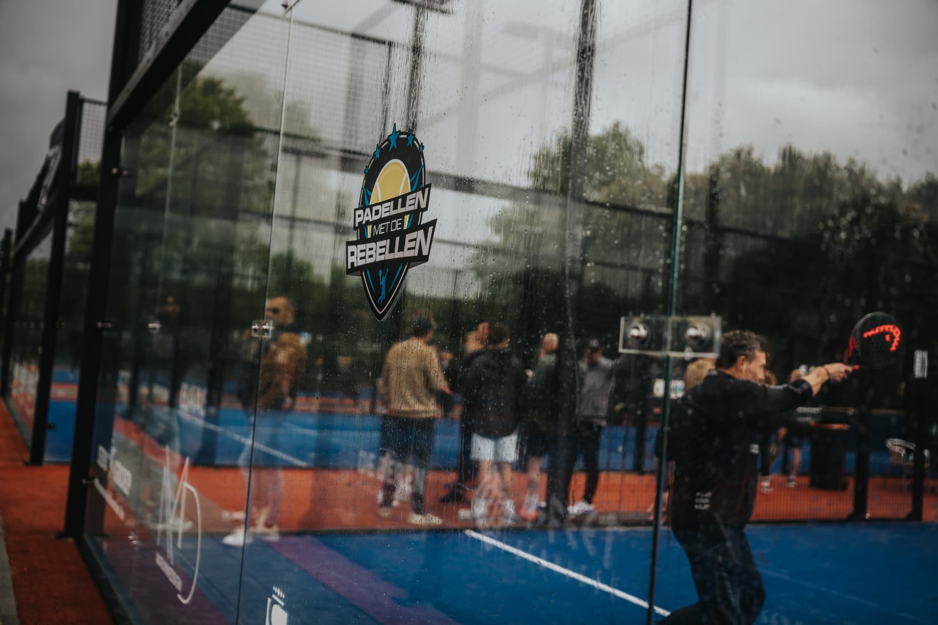 Het logo van Padellen met de Rebellen op de glaswand van een padelbaan