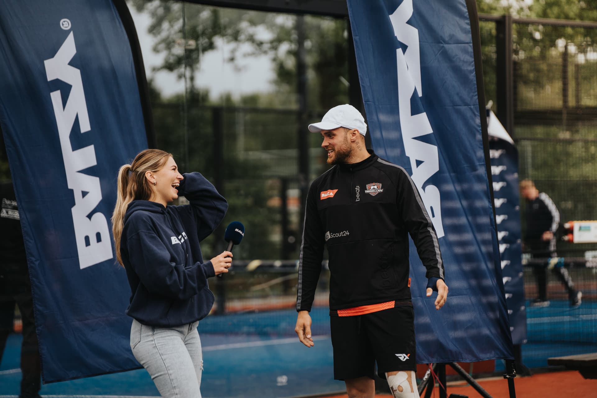 Interview met een speler tussen twee sponsorvlaggen naast de baan