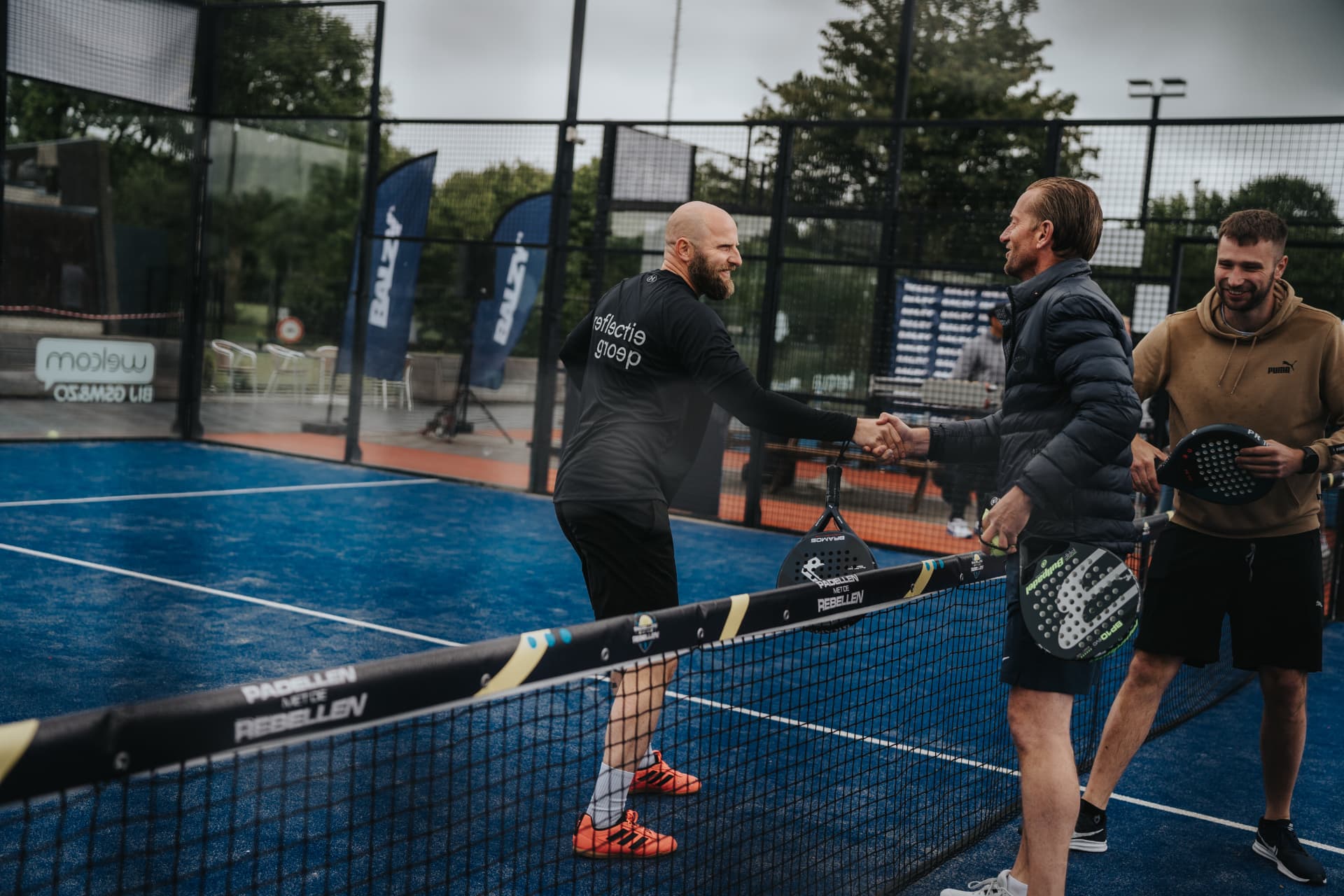 Twee spelers schudden handen over het net terwijl teamgenoten toekijken