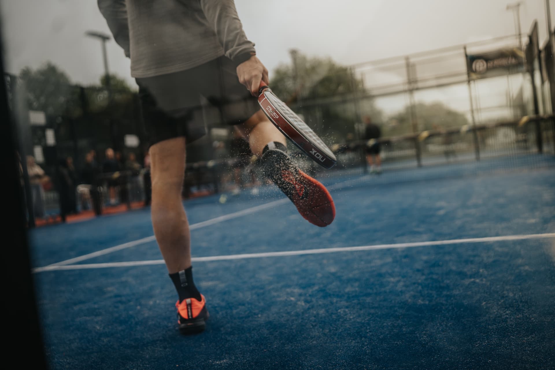 Speler slaat een lage bal terug op een blauwe padelbaan