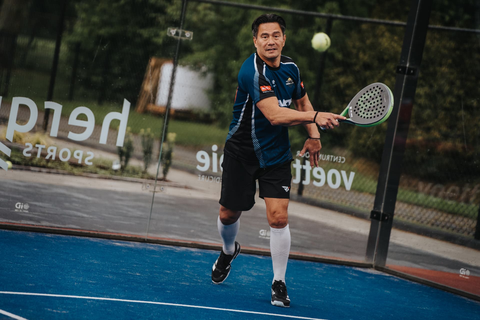 Speler slaat een forehand op de blauwe padelbaan
