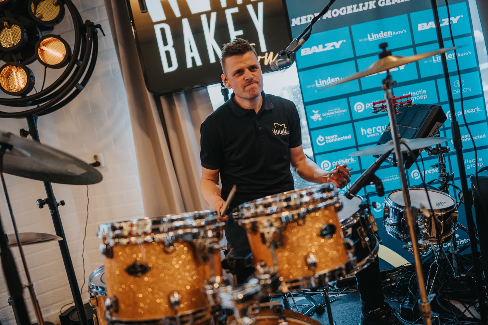 Drummer van de band Bakey Town speelt op een goudkleurig drumstel voor de sponsorwand
